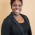 African American female with short dark pink hair wearing a black dress & blazer w/ silver necklace